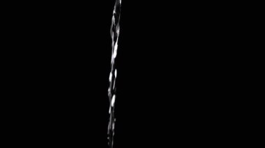 Thin Stream Of Water Pouring On Black Background. Close-up, slow motion. A clear stream of water flows down into empty space. Splashes. Abstract, texture, lighting. Clean water.