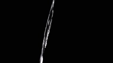 Thin Stream Of Water Pouring On Black Background. Close-up, slow motion. A clear stream of water flows down into empty space. Splashes. Abstract, texture, lighting. Clean water.