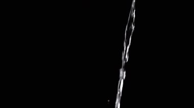 Yan görüş, İnce Su Akıntısı Siyah Arkaplan 'a dökülüyor. Yakın çekim, yavaş çekim. Temiz bir su akıntısı boşluğa akar. Sıçramalar. Soyut, desen, aydınlatma. Temiz su.