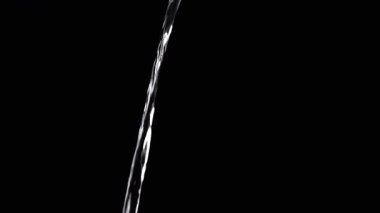 Thin Stream Of Water Pouring On Black Background. Close-up, slow motion. A clear stream of water flows down into empty space. Splashes. Abstract, texture, lighting. Clean water.