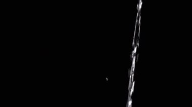 Thin Stream Of Water Pouring On Black Background. Close-up, slow motion. A clear stream of water flows down into empty space. Splashes. Abstract, texture, lighting. Clean water.