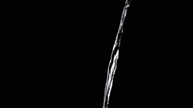 Thin Stream Of Water Pouring On Black Background. Close-up, slow motion. A clear stream of water flows down into empty space. Splashes. Abstract, texture, lighting. Clean water.