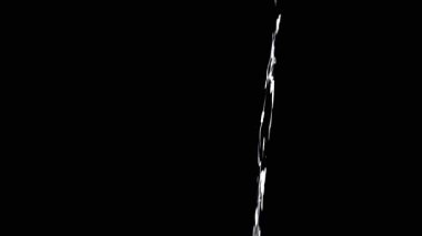Thin Stream Of Water Pouring On Black Background. Close-up, slow motion. A clear stream of water flows down into empty space. Splashes. Abstract, texture, lighting. Clean water.