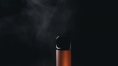 Yakın plan, Elektronik Sigara veya Siyah Arkaplanda Tüttüren Vape. Karanlık bir ortamda ortaya çıkan dumanlı tek bir cisim gizemli bir atmosfer yaratıyor. Doku. Bulanık hareket.