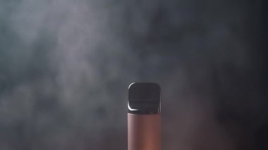 Yakın plan, Elektronik Sigara veya Siyah Arkaplanda Tüttüren Vape. Karanlık bir ortamda ortaya çıkan dumanlı tek bir cisim gizemli bir atmosfer yaratıyor. Doku. Bulanık hareket.