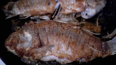 Kızarmış balık, sıcak bir tavada cızırdıyor. Lezzetli bir yemek sergiliyor.