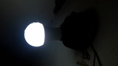 Parlak beyaz bir LED ampul koyu gölgeli bir tavana karşı yoğun bir şekilde parlar. Açıkta duran kablolar, aydınlık ve karanlık arasında katı bir zıtlık yaratıyor..