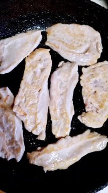 Sıcak siyah bir tavada kızaran dilimlenmiş tavuk göğsü filetolarının yakın çekim görüntüsü. Kümes hayvanları yağda cızırdıyor, fırında pişerken çiğ pembeden beyaza dönüyorlar..