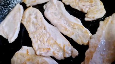 Siyah tavada pişen dilimlenmiş tavuk göğsü filetolarının yukarıdan aşağı görüntüsü. Et tavada cızırdarken altın sarısı kavurucu kenarlarıyla beyazlaşıyor..