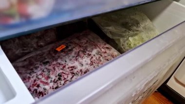 Açık bir buzdolabı çekmecesinin elektrikle mühürlenmiş doğranmış donmuş sebzelerle dolu statik yakın plan görüntüleri. Bir poşette kırmızı pancar ve sebze karışımı var..