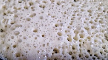 Makro yakın plan krep hamuru tavada pişiyor. Kabarcıklar sürekli şekillenir, doğar ve hamur yüzeyinde patlar, gözenekli, süngerimsi bir doku oluşturarak ısınır ve kızarır..