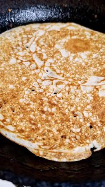 Koyu, yapışmaz tavada pişen gözenekli gözlemenin dikey, makro yakın çekim görüntüsü. Altın-kahverengi yüzey kızarırken küçük kabarcıklarla kaplıdır, pişirme sürecini gösterir..