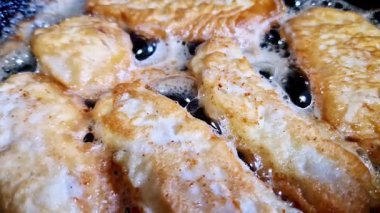 Siyah bir tavada kaynayan kızgın yağda kızaran altın ve ekmek kırıntılarının yukarıdan görünüşü. Bu makro perspektif, ev yapımı bir mutfak sahnesinde yemek hazırlama sürecini gösterir..