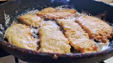 Çıtır, altın sarısı, kahverengi balık filetolarının, dökme demir bir tavanın içinde kızgın yağda kızarmasının orta açı görüntüsü. Cızırdayan yağ, ev yapımı akşam yemeği için nefis bir mutfak hazırlığı gösteriyor..