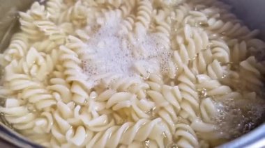 Kaynayan suyun içinde kaynayan fusilli makarna yakın çekim. Beyaz, nişasta köpüğü ve kabarcıklar sıvının yüzeyine yükselir, ham maddelerden bir yemek hazırlama sürecini gösterir..
