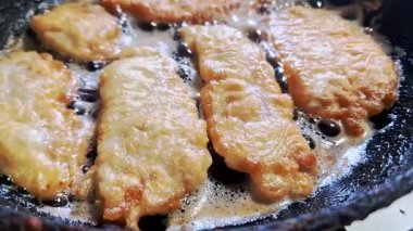 Aşırı derecede yakın plan altın-kahverengi balık filetoları cızırdıyor ve kızgın, köpüren yağda kızarıyor. Mutfak pişirme işlemi sırasında tava yüzeyinde çıtır çıtır tabakanın detaylı dokusu görülebilir..