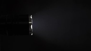 Taktik el feneri, havada yüzen toz parçacıklarını aydınlatan parlak bir ışın yayar. Siyah arka planda çekilen sahnenin gizemli ve ürkütücü bir atmosferi var..