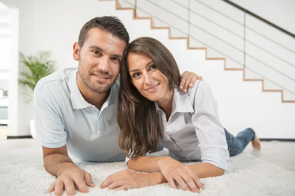 Cheerful young couple laying on carpet floor — Stock Photo, Image