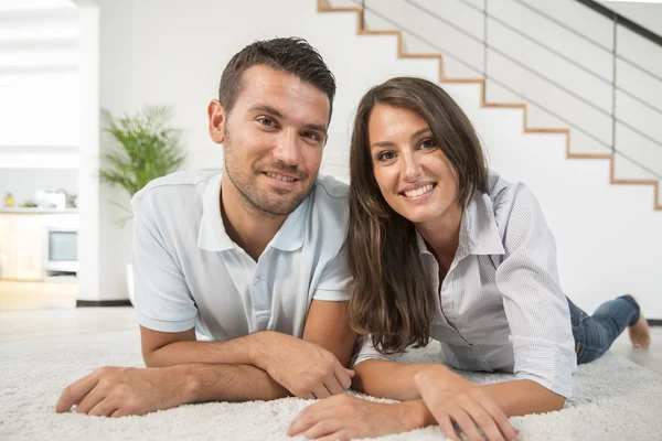 Cheerful young couple laying on carpet floor — Stock Photo, Image