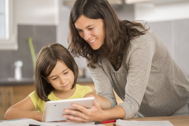 Anne ve kızı tabletle ödev yapıyor.