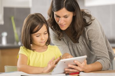 Anne ve kızı tabletle ödev yapıyor.