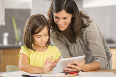 Anne ve kızı tabletle ödev yapıyor.