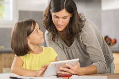 Anne ve kızı tabletle ödev yapıyor.