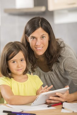 Anne ve kızı tabletle ödev yapıyor.