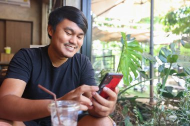 Kafede akıllı telefon kullanan Asyalı bir adamın portresi. Kahve dükkanında gülümseyen adam..