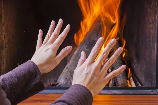 Woman warming hands at fireplace — Stock Photo, Image