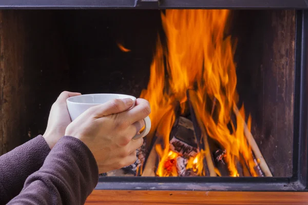 Opwarming van de aarde handen bij open haard met koffie en thee — Stockfoto