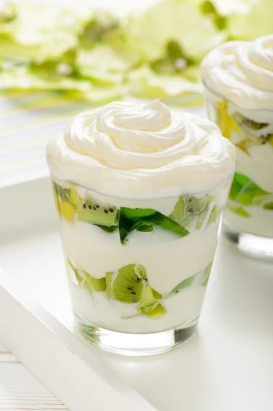 Gesundes Joghurt-Dessert mit Kiwi-Früchten, Gelee und Sahne im Glas auf weißem Holztablett. — Stockfoto
