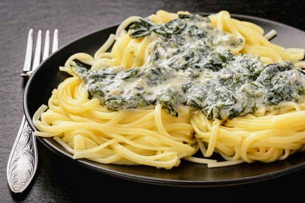 Italian pasta with spinach sauce on black plate. — Stock Photo, Image