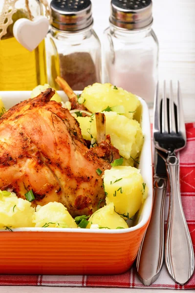 Oven baked rabbit with potatoes  in orange ceramic bowl on white  wooden table.