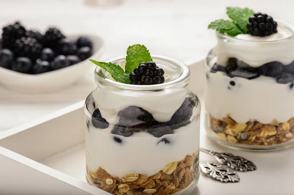 Gesundes Joghurt-Dessert mit Müsli, Brombeeren und Blaubeeren auf weißem Holztisch. — Stockfoto