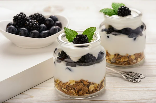 Sobremesa de iogurte saudável com muesli, amoras e mirtilos na mesa de madeira branca . — Fotografia de Stock