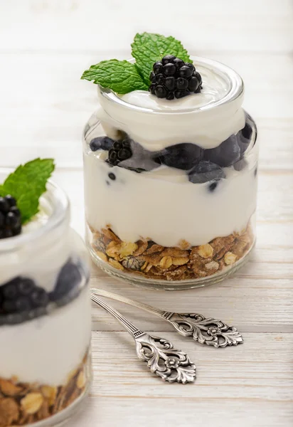 Gesundes Joghurt-Dessert mit Müsli, Brombeeren und Blaubeeren auf weißem Holztisch. — Stockfoto