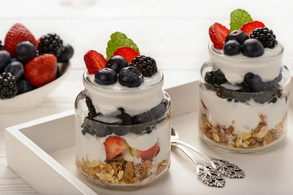 Gesundes Joghurt-Dessert mit Müsli, Erdbeeren, Brombeeren und Blaubeeren auf weißem Holztisch. — Stockfoto