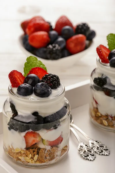 Gesundes Joghurt-Dessert mit Müsli, Erdbeeren, Brombeeren und Blaubeeren auf weißem Holztisch. — Stockfoto