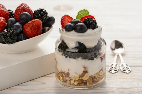 Sobremesa de iogurte saudável com muesli, morangos, amoras e mirtilos na mesa de madeira branca . — Fotografia de Stock