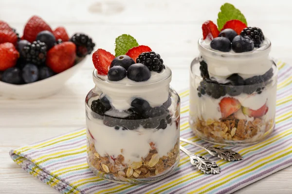 Gesundes Joghurt-Dessert mit Müsli, Erdbeeren, Brombeeren und Blaubeeren auf weißem Holztisch. — Stockfoto