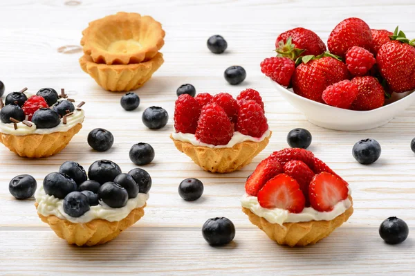 Tartaletas con crema, arándanos, frambuesas y fresas sobre mesa de madera blanca. Enfoque selectivo . — Foto de Stock
