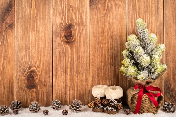 Decoratieve fir-kerstboom met laarzen en kegels op de gesneeuwde houten achtergrond. — Stockfoto