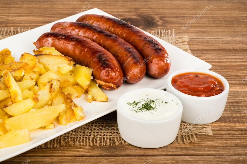 Grilled sausages and fried potatoes on the white plate on the rustic