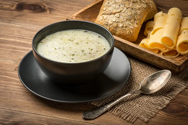 Käsesuppe und schwarze Schüssel auf rustikalem Holzgrund. — Stockfoto