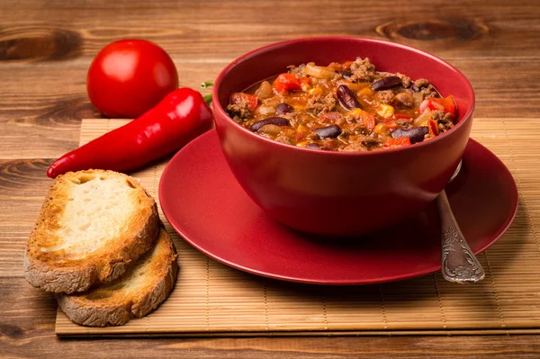 Chili con Corne serviert in der roten Schüssel auf dem hölzernen Hintergrund. — Stockfoto