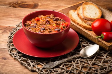 Ahşap arka plan üzerinde kırmızı kase Chili con carne hizmet.
