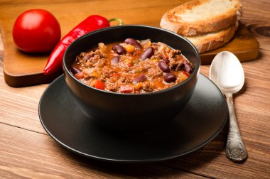 Ahşap arka plan üzerinde siyah kase Chili con carne hizmet.