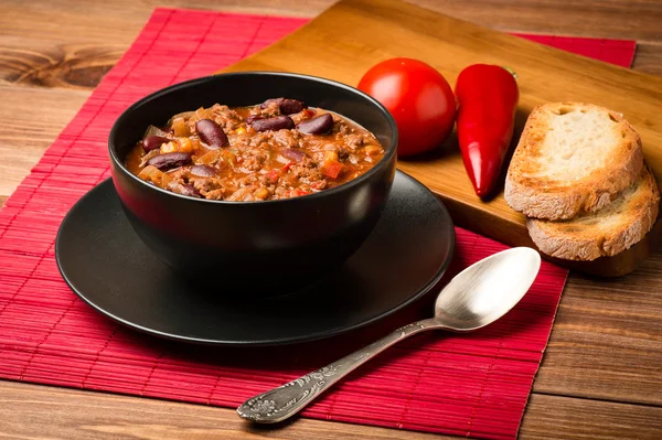 Chili con Corne serviert in der schwarzen Schüssel auf dem hölzernen Hintergrund. — Stockfoto