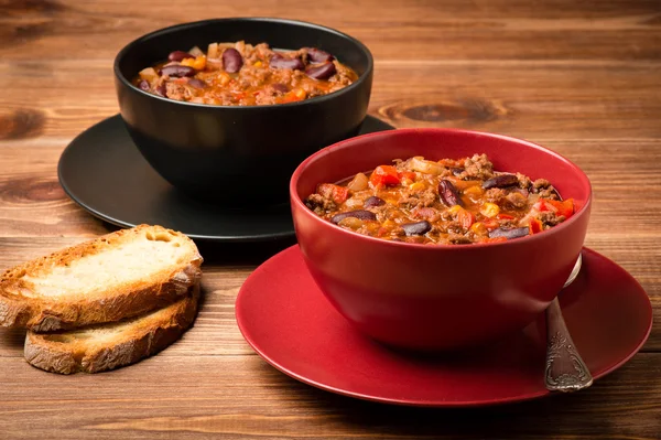 Chili con Corne serviert in den roten und schwarzen Schüsseln auf dem Holzhintergrund. — Stockfoto